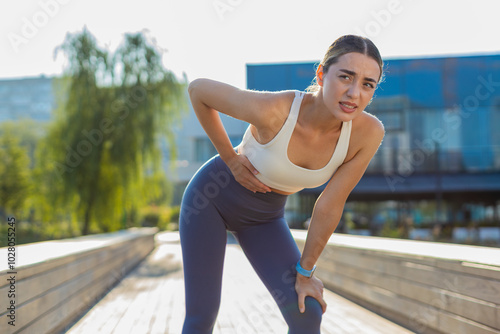 Photography Young Caucasian runner suffering from abdominal pain during a run in urban city park on sunny day