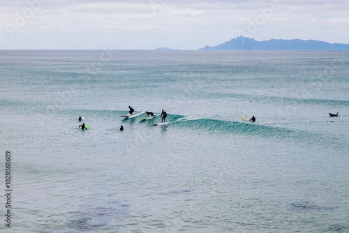 People surfing on longboards in calm ocean waves on a sunny day at Te Arai Beach, Auckland, New Zealand. photo