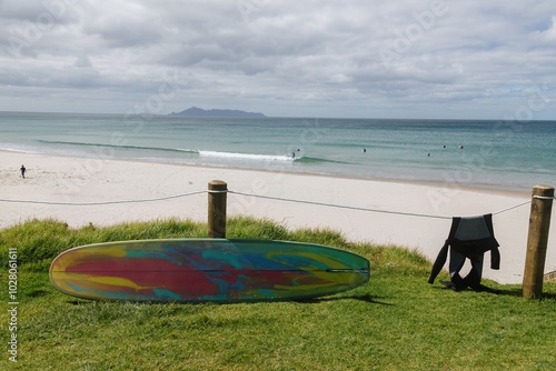 Surfboard leaning up against a fencepost and wet suit drying on a calm sunny day at Te Arai Beach, Auckland, New Zealand. photo