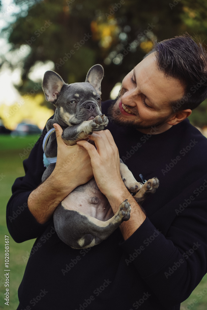 Obraz premium man hugging a dog, walk in the park, outside french bulldog puppy with owner, man with pet spending time outside the house, happy smiling people with a dog