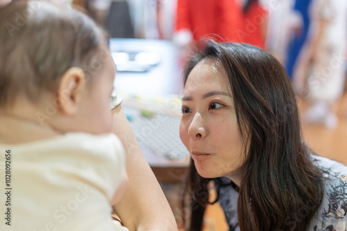 Quadro em tela A Taiwanese woman in her 30s wearing traditional Chinese clothing is entertaining a 6-month-old baby being held by another woman on Dihua Street in Taipei City, Taiwan, in September