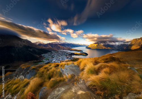 A panoramic view from a mountaintop overlooking a town, a lake, and snow capped mountains.