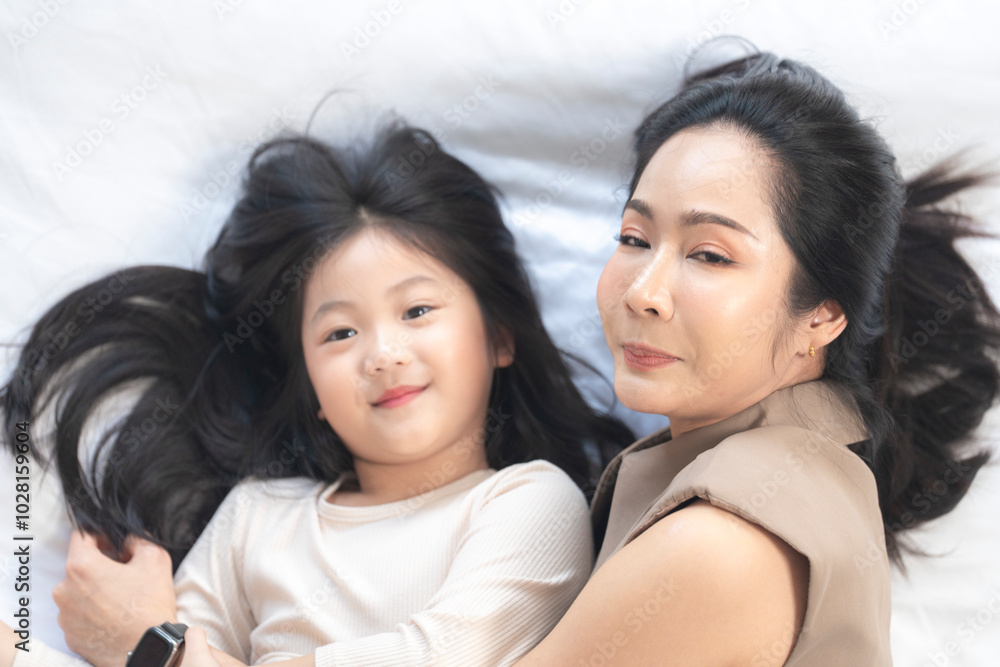 A joyful mother and daughter laughing together while lying on a bed. The playful moment showcases their strong bond and happiness in a comfortable home setting, surrounded by natural decor. A joyful mother and daughter laughing together while lying on a bed. The playful moment showcases their strong bond and happiness in a comfortable home setting, surrounded by natural decor.