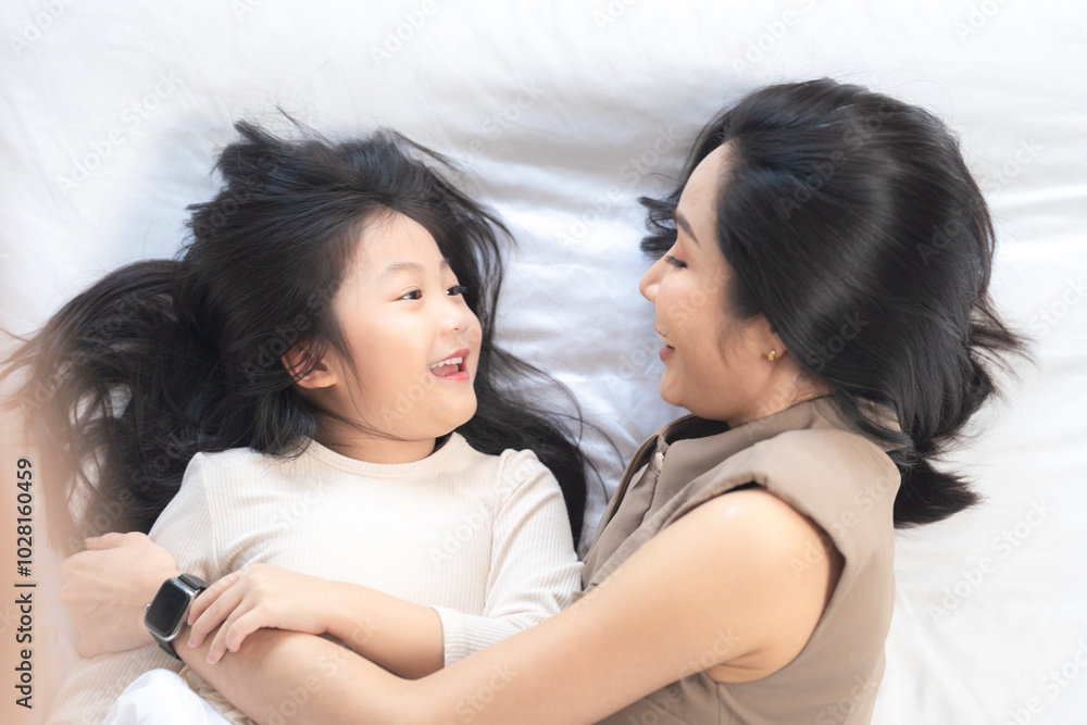 A joyful mother and daughter laughing together while lying on a bed. The playful moment showcases their strong bond and happiness in a comfortable home setting, surrounded by natural decor. A joyful mother and daughter laughing together while lying on a bed. The playful moment showcases their strong bond and happiness in a comfortable home setting, surrounded by natural decor.