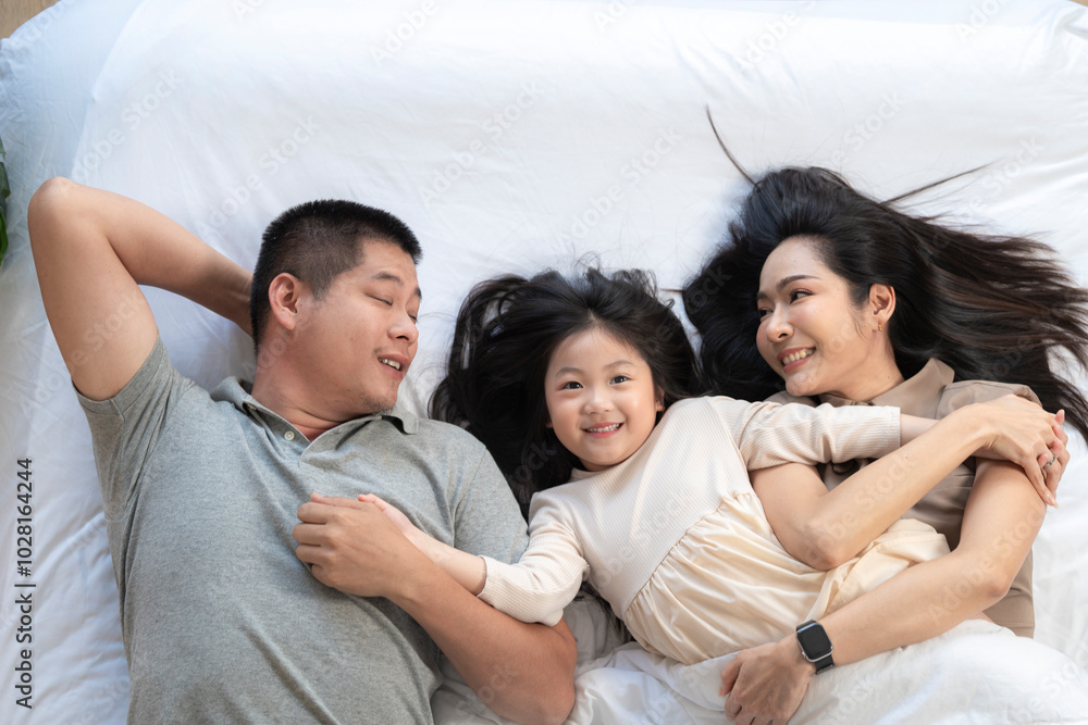 Obraz premium A joyful mother and daughter laughing together while lying on a bed. The playful moment showcases their strong bond and happiness in a comfortable home setting, surrounded by natural decor.