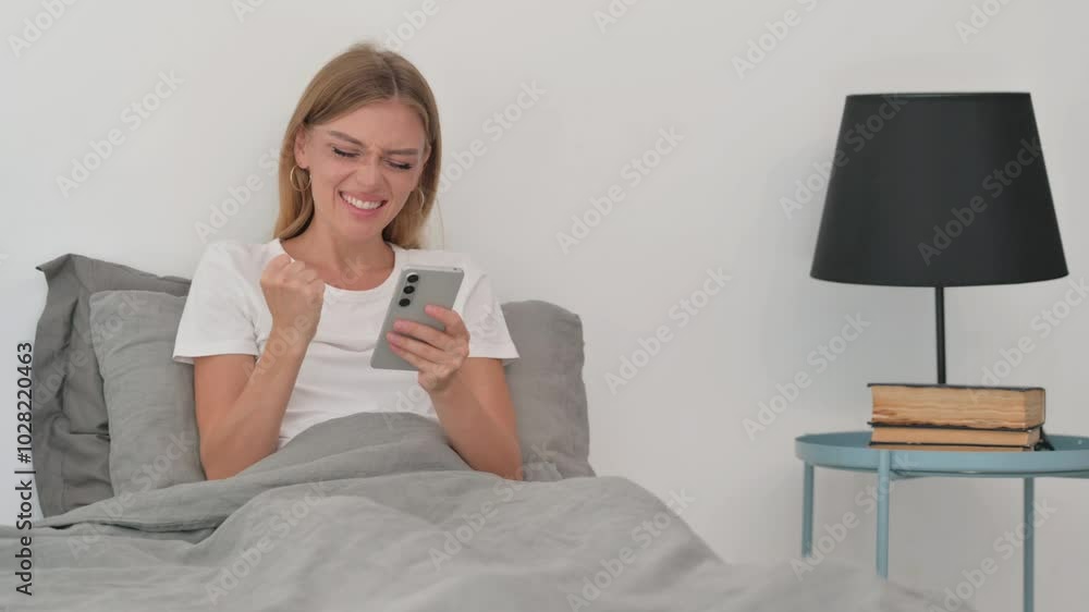 Young Woman Celebrating Success on Phone while Sitting in Bed Young Woman Celebrating Success on Phone while Sitting in Bed