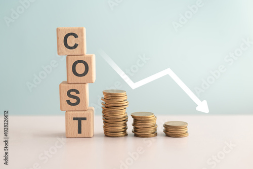 For reduction concept which effect to product cost , profit , inflation and economy recession concept, COST text on wooden cube blocks, stack of coins and decreasing graph