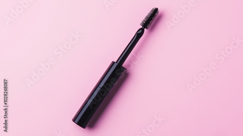 A single black mascara wand and its tube against a pink background.