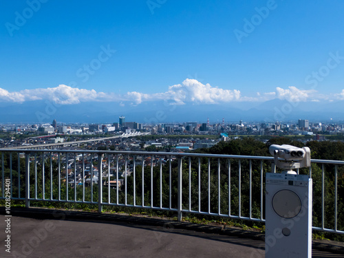 呉羽山展望台の望遠鏡と眼下に広がる富山市市街地と北アルプスの白い雲浮かぶ