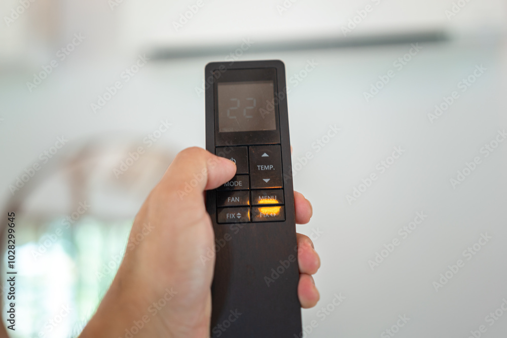 Human hand is turning-on air conditioner by pressing the button on remote control. Home appliance and interior object, close-up and selective focus. Human hand is turning-on air conditioner by pressing the button on remote control. Home appliance and interior object, close-up and selective focus.
