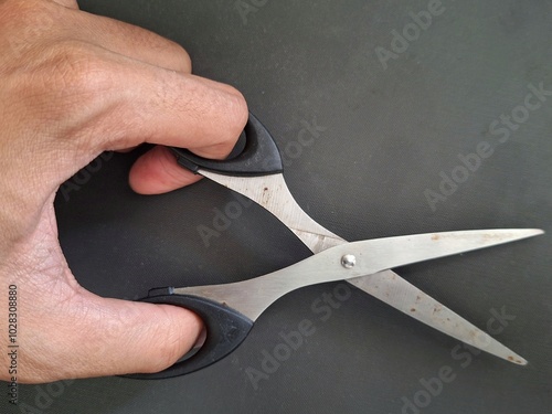 Man's hand holding used scissors in open position on black dark gray background