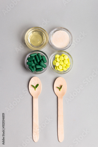 Homeopathic medicine. Homeopathic pills in a glass bowls, green leaves on wooden spoons from above on a light grey background. Alternative medicines top view.