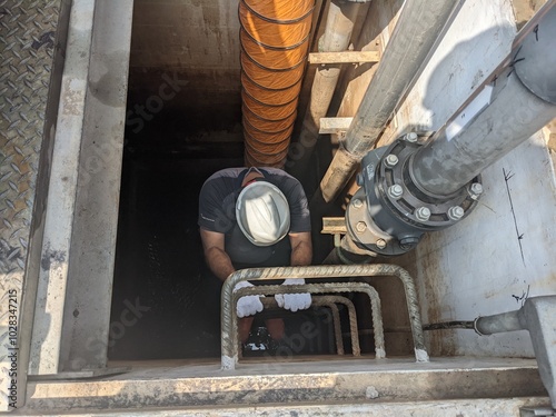 Worker Descending into a Manhole for Inspection and Maintenance, confine space. A worker wearing safety gear descends into a manhole for inspection and maintenance of underground utility systems. photo