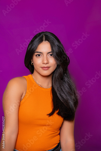 Thoughtful woman in casual orange top and jeans with relaxed expression, purple backdrop