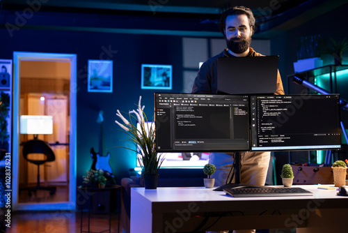 Cybersecurity expert using laptop to look for company security vulnerabilities, comparing with computer monitors. Programmer installing fortified code on laptop, crosschecking with PC screens photo