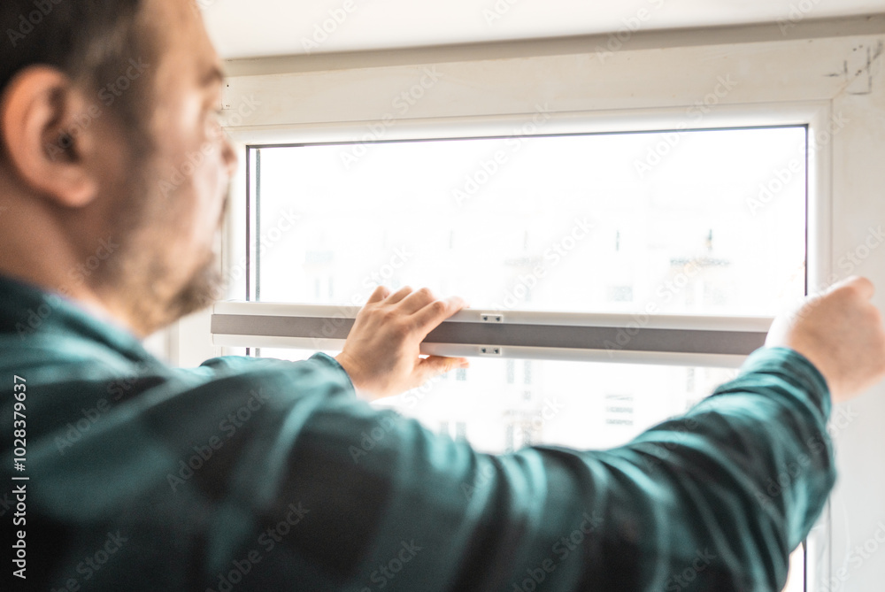Fototapeta premium Man installs roller blinds. Handyman mesures window to fix it.
