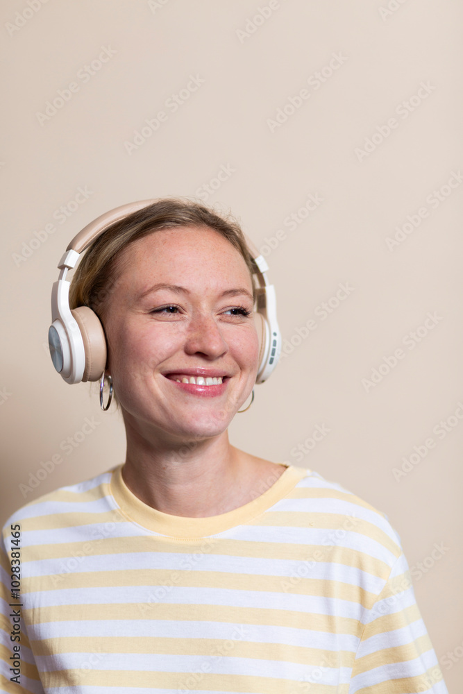 Smiling blond woman wearing headphones against beige background Smiling blond woman wearing headphones against beige background