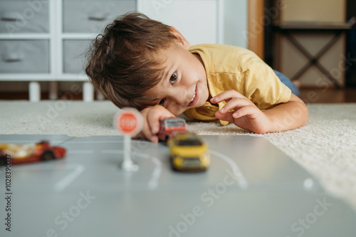 Cute boy lying down and playing with toy car at home photo