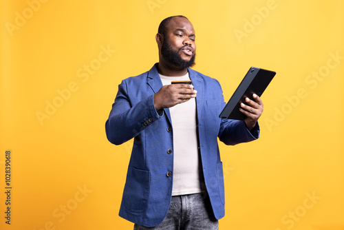 Annoyed BIPOC man irritated after seeing insufficient funds error while trying to buy stuff online. Upset person getting transaction rejected on tablet, isolated over studio background photo