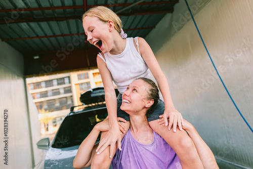 Mother carrying cheerful daughter on her shoulders at car washing station photo