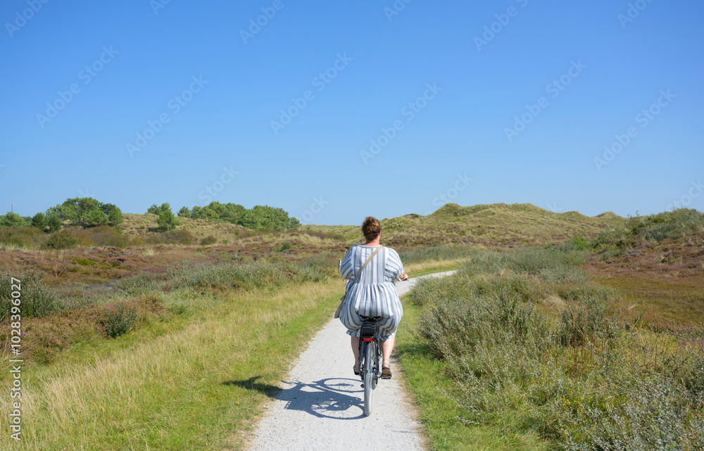 Woman riding bicycle on road amidst plants under blue sky Woman riding bicycle on road amidst plants under blue sky