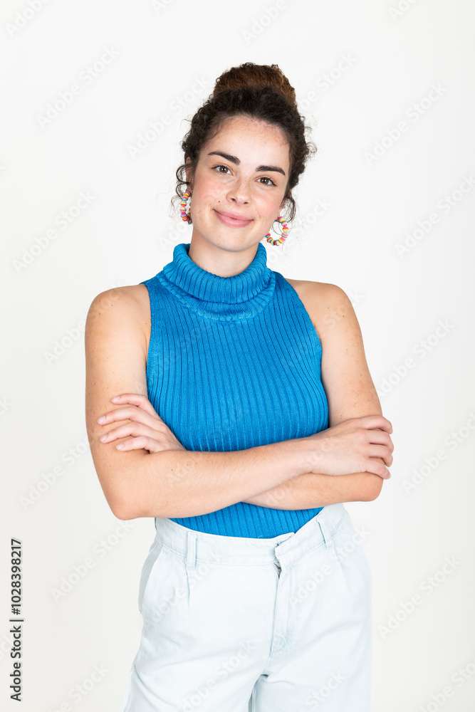 Smiling young woman wearing blue turtleneck t-shirt and standing with arms crossed against white background Smiling young woman wearing blue turtleneck t-shirt and standing with arms crossed against white background