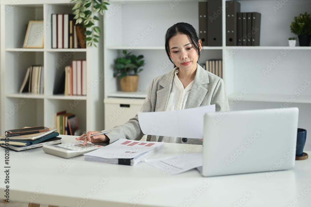 Attractive female accountant reviewing documents and using a calculator at desk Attractive female accountant reviewing documents and using a calculator at desk