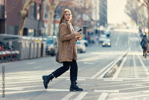 Young woman holding smart phone and crossing road at crosswalk photo