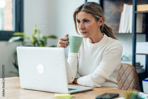 Mature businesswoman having coffee and using laptop at work place