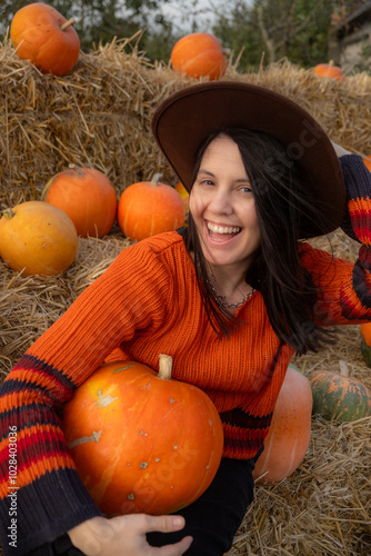 Woman holding a pumpkin sitting on hay bales