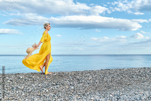 Mature woman with straw hat walking by coastline at beach photo