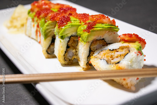 Close up of sushi roll with fried shrimp inside and fresh avocado and salmon on the top