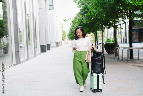 Woman using smart phone and walking with luggage in city photo