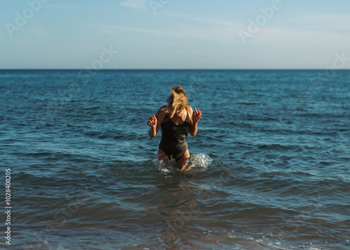 A woman stands in the sea in a swimsuit.