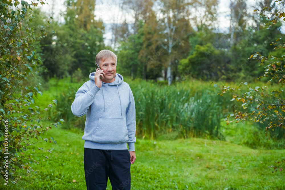 Man in hoodie with mobile phone resting after training in park Man in hoodie with mobile phone resting after training in park