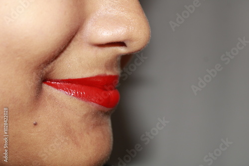 Vibrant red lips curve upwards in a joyful smile. Perfect natural lip makeup. Close up macro photo with beautiful Indian teenage girl mouth.