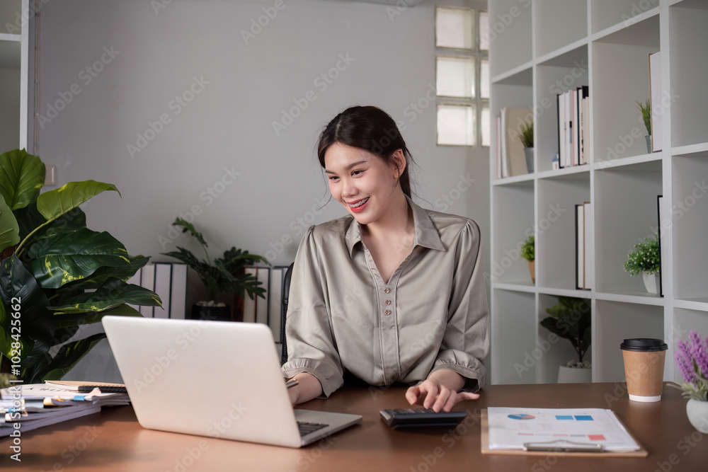 Fototapeta premium Businesswoman Working on Laptop in Modern Office with Plants and Documents on Desk