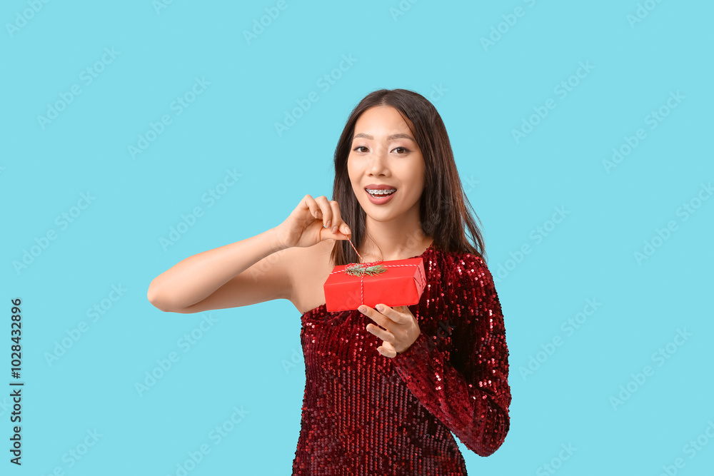Young Asian woman with Christmas gift box on blue background Young Asian woman with Christmas gift box on blue background