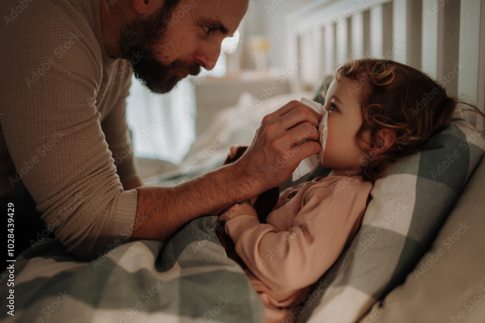 Sick girl with cold lying in the bed. Father helping little daughter to blow her nose. Sick girl with cold lying in the bed. Father helping little daughter to blow her nose.