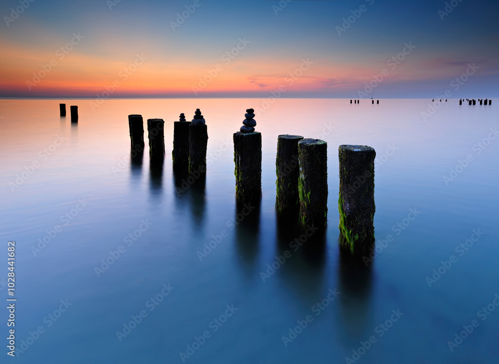 Old Wooden Groyne with stacks of balanced stones in the water of the baltic sea at sunset