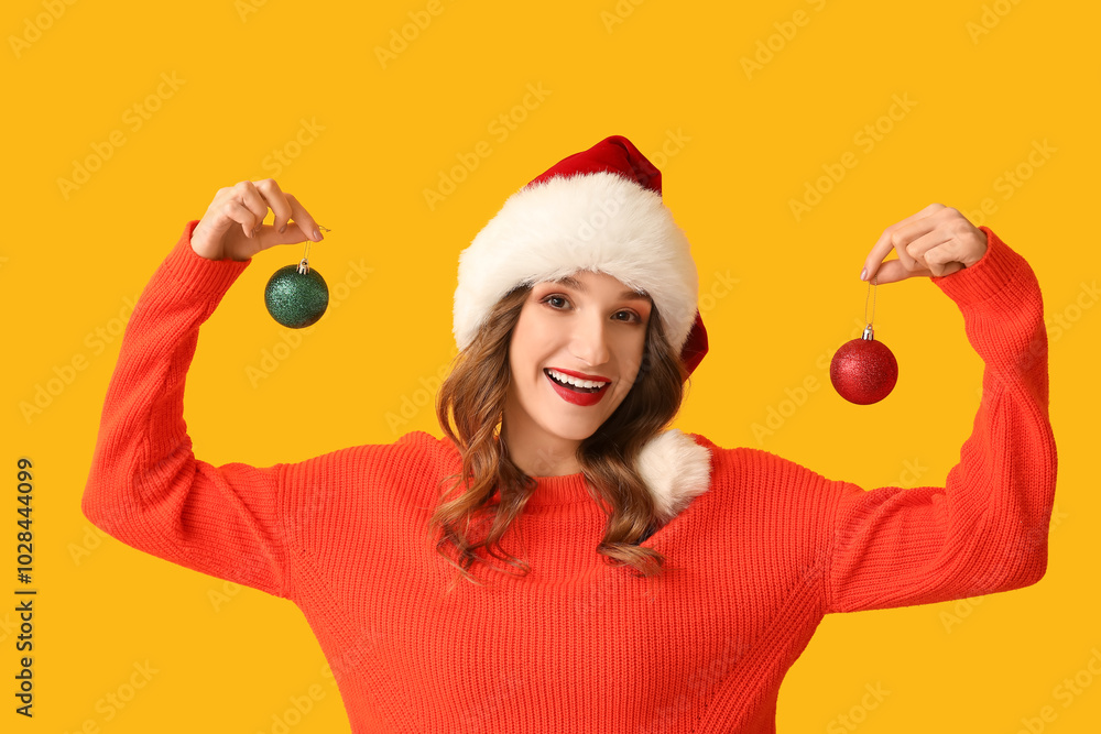 Young woman in Santa hat with Christmas balls on yellow background Young woman in Santa hat with Christmas balls on yellow background