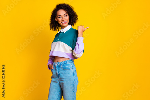 Photo of positive woman with curly hair dressed striped top look directing at proposition empty space isolated on yellow color background photo