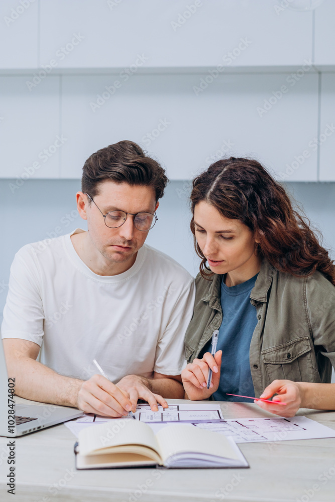 Young couple is deeply engrossed in designing the layout of their future home, carefully considering each detail on the blueprints Young couple is deeply engrossed in designing the layout of their future home, carefully considering each detail on the blueprints