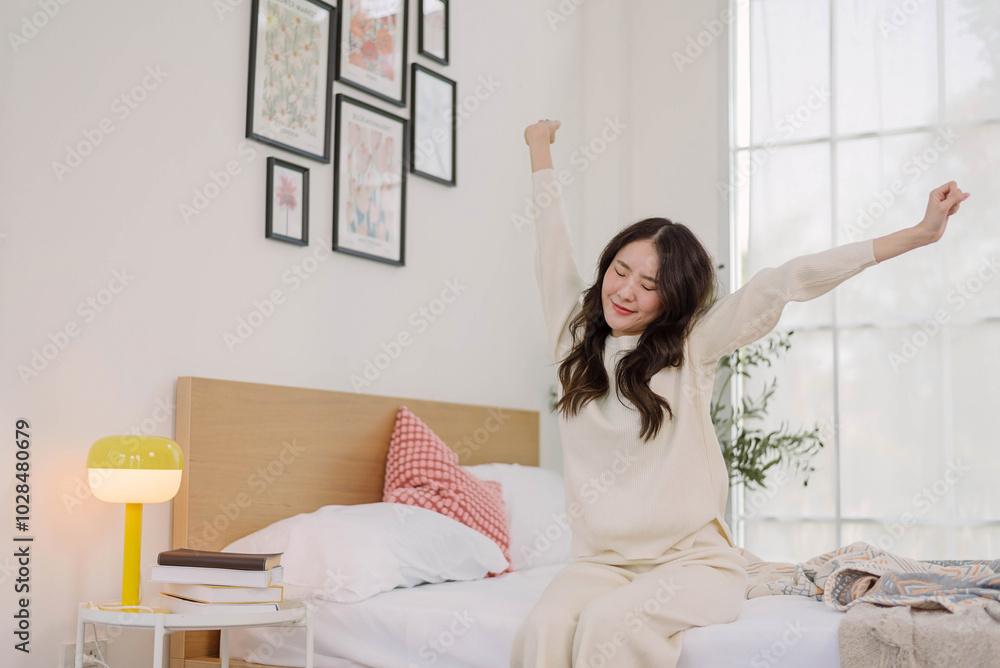 Asian woman in cozy attire Stretching after wake-up on a bed in bedroom with a morning warm ambiance.