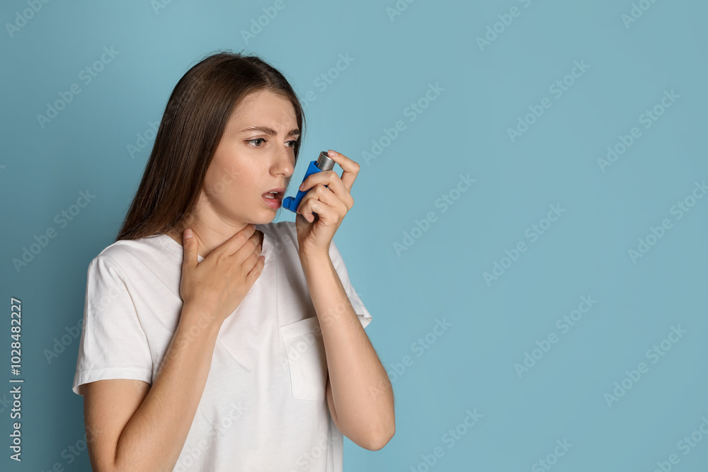 Young woman using asthma inhaler on light blue background. Space for text Young woman using asthma inhaler on light blue background. Space for text