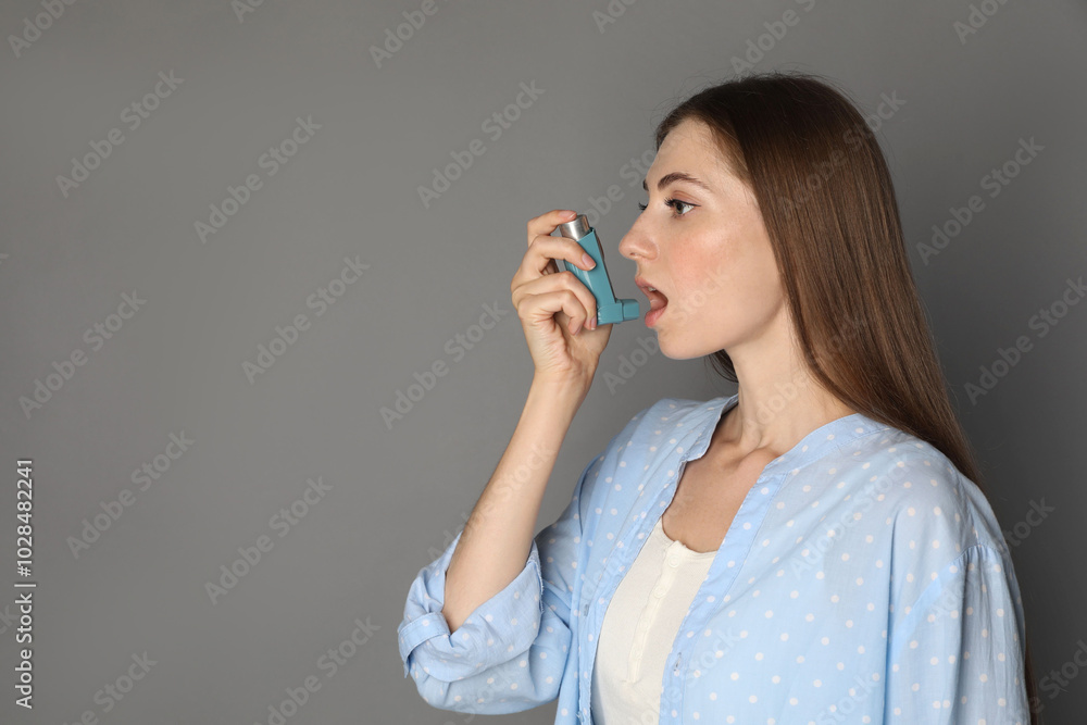 Young woman using asthma inhaler on grey background. Space for text Young woman using asthma inhaler on grey background. Space for text