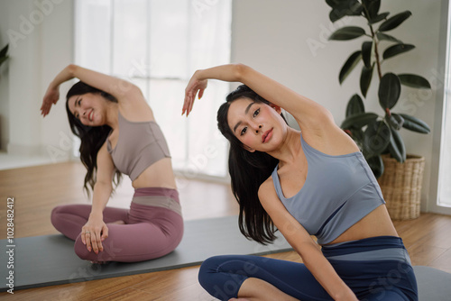 Two Asian woman wearing sportwear practicing yoga at home studio. Health care and wellness activities.