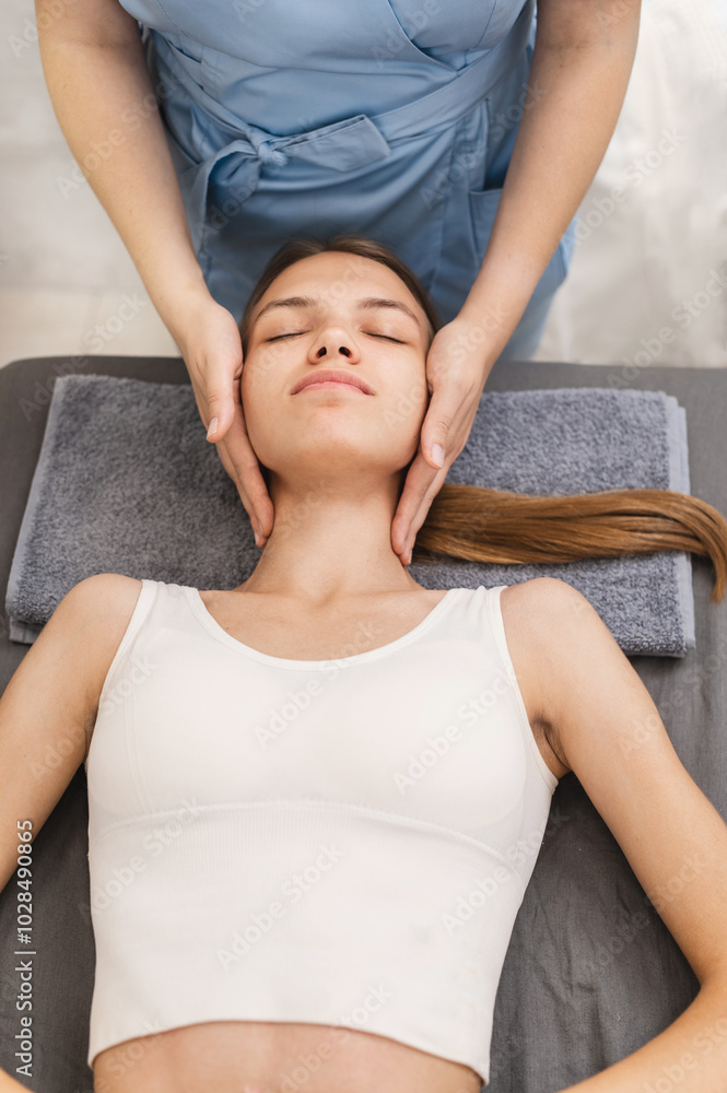 Naklejka premium Relaxing massage in the spa salon. Skin care and rest. woman getting massaging treatment over grey towel. Spa, healthcare and recreation concept. portrait closeup top view
