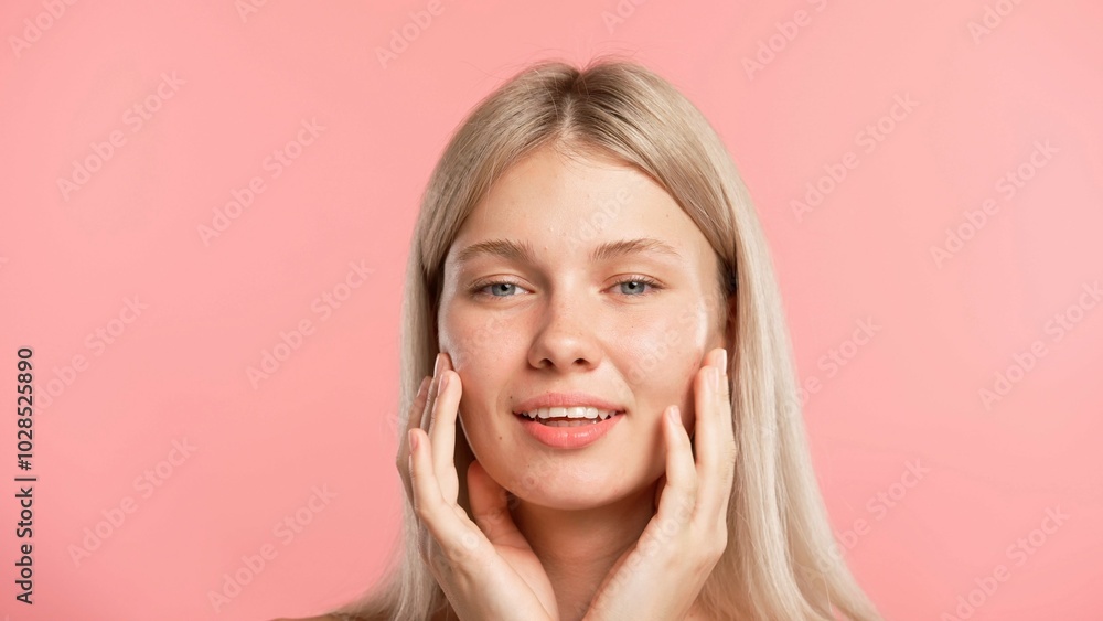 Young blonde woman posing at camera, looks playfully smiling and touches skin, isolated on pink studio background. Beauty skin care concept Young blonde woman posing at camera, looks playfully smiling and touches skin, isolated on pink studio background. Beauty skin care concept