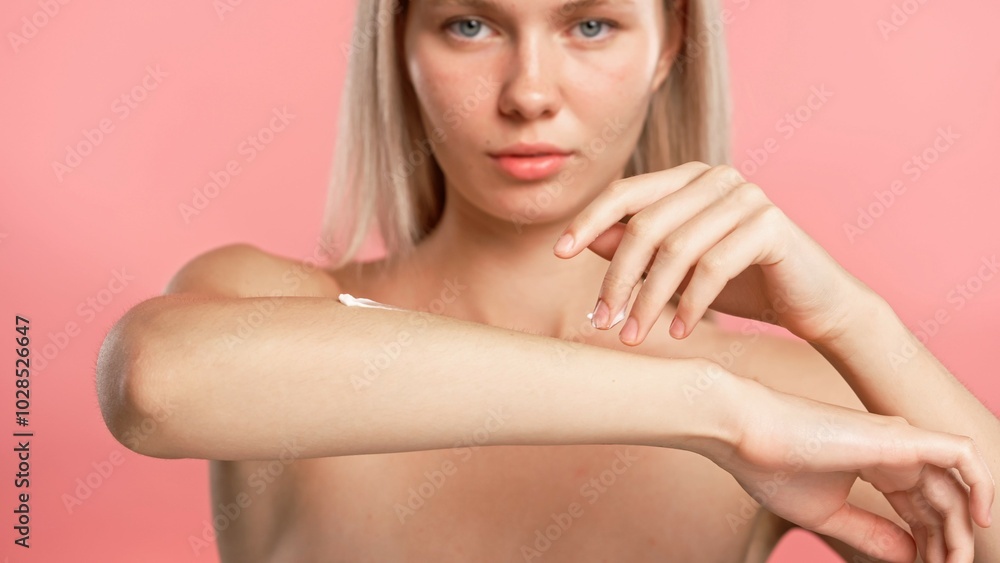 Young blonde woman posing at camera, applying body cream on arm, isolated on pink studio background close up shot. Beauty skin care concept Young blonde woman posing at camera, applying body cream on arm, isolated on pink studio background close up shot. Beauty skin care concept